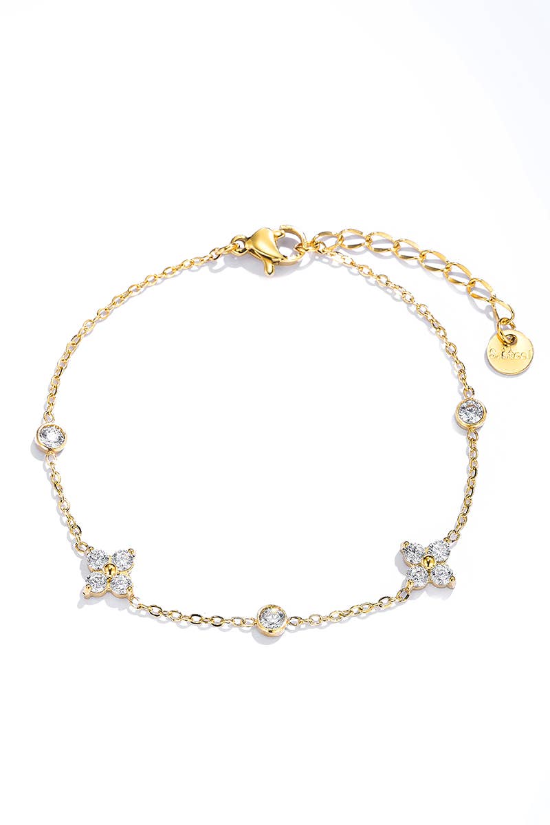 Gold bracelet with floral and round charms on a white background